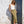 Woman in a white top and green skirt standing against a white wall with a dark doorway.