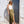 Woman in a white top and green skirt standing against a white wall with an arched doorway.