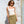 Woman wearing a white top and green skirt standing against a textured white wall.
