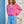 Woman wearing a pink sweater and blue jeans standing against a textured wall.