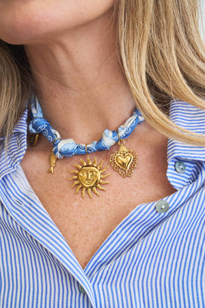 Necklace with sun and heart pendants on a person wearing a blue and white striped shirt.