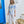 Jess Dempsey wearing a blue and white abstract patterned shirt and white pants standing in front of a blue door.
